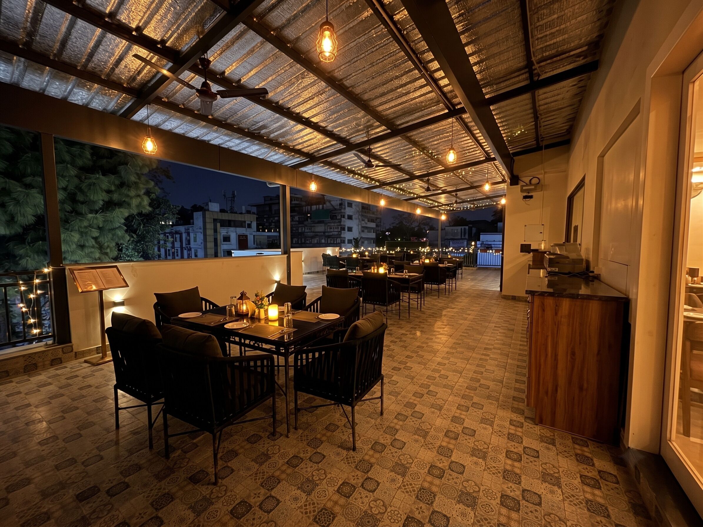 An indoor dining area with tables and chairs, a ceiling with a grid-like pattern, and a view of buildings outside.