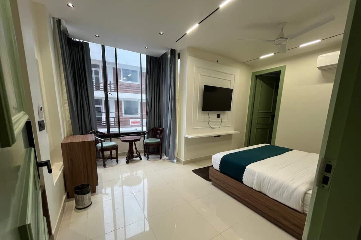 A hotel room with a bed, a TV mounted on the wall, a desk with a chair, and a window with curtains.