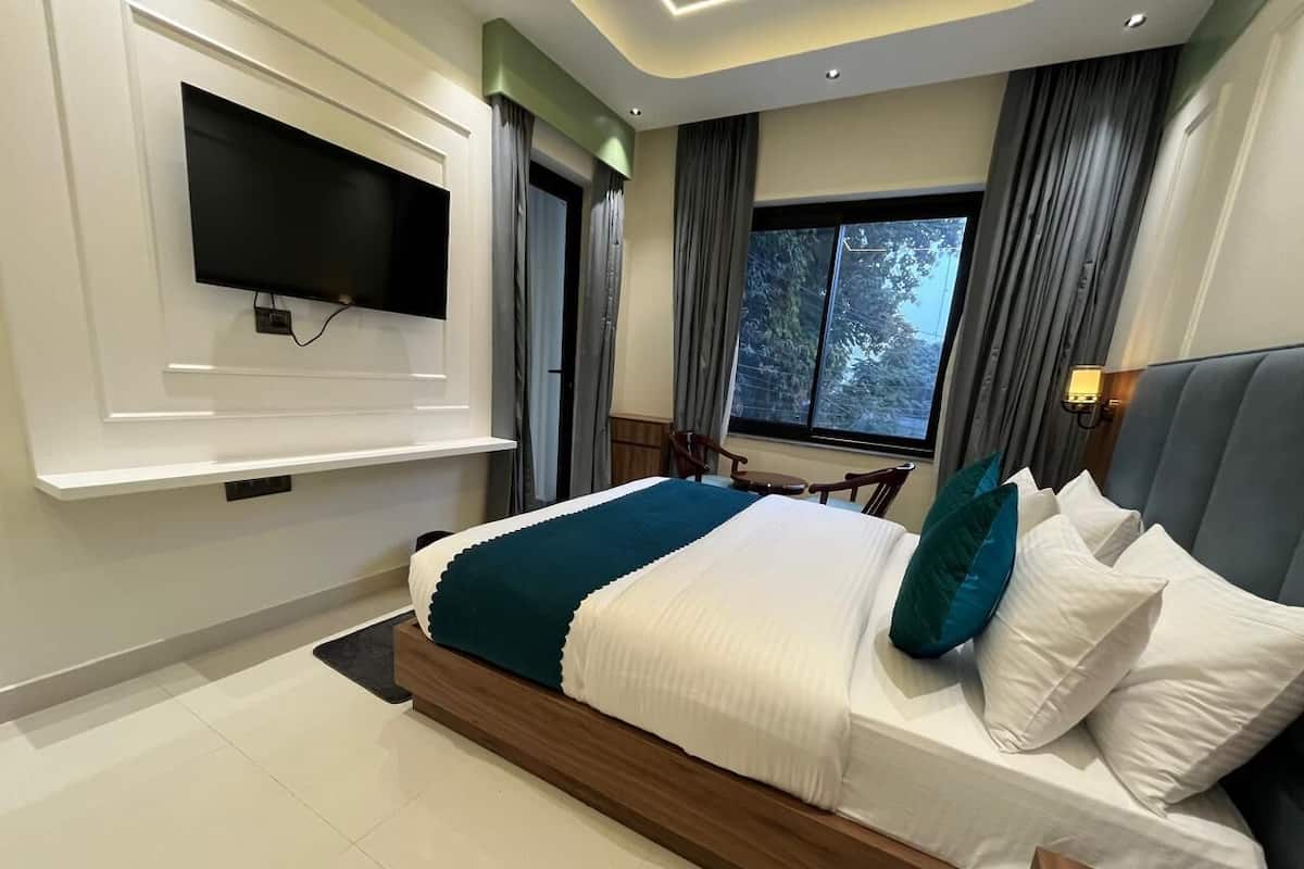 Un dormitorio moderno con una cama grande, un televisor montado y una ventana con cortinas.