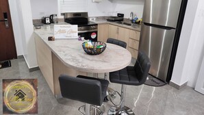 Una cocina moderna con un refrigerador de acero inoxidable, un horno empotrado y un microondas. Hay un letrero en la encimera que dice "The Simpsons' Little Gem".