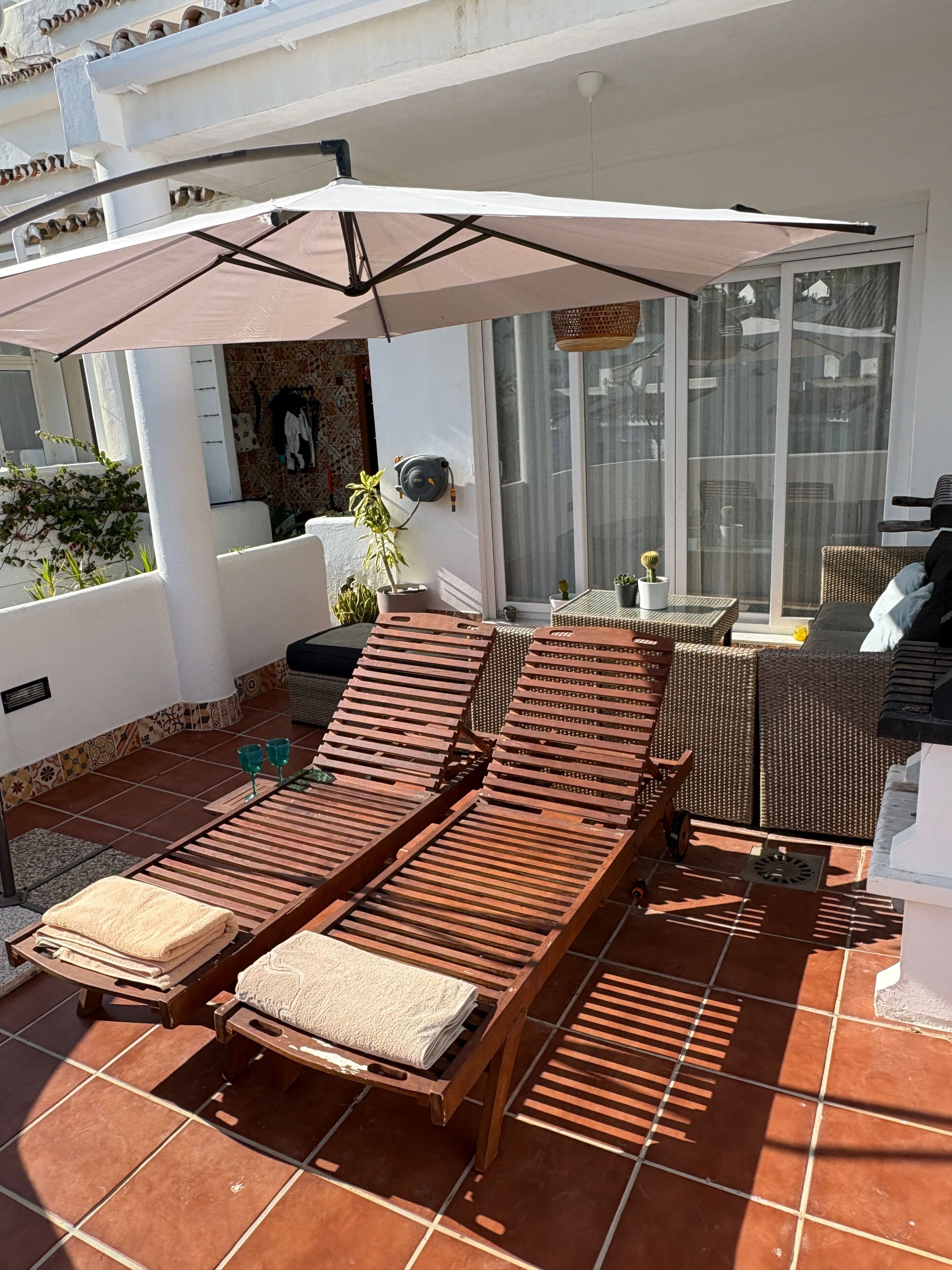 A terrace with wooden loungers, a large umbrella, and a view of the city.