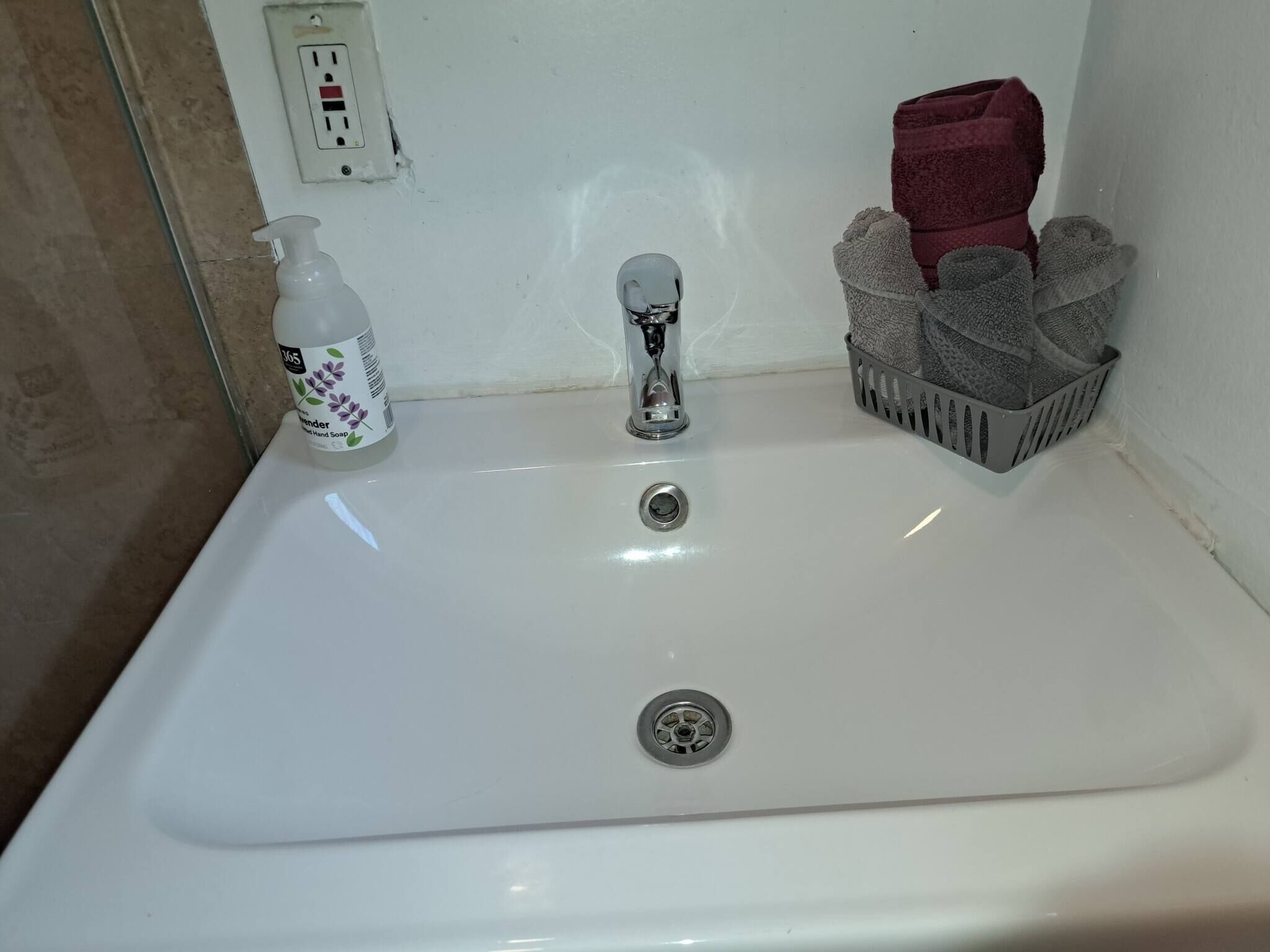 A bathroom sink with a bottle of hand soap, a faucet, and a towel rack with towels.