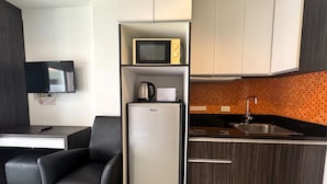 Una cucina compatta con forno a microonde, bollitore e lavello. Include un piccolo frigorifero e un televisore a schermo piatto montato a parete.