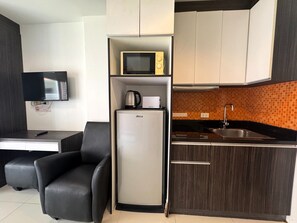 A compact kitchenette with a microwave, kettle, and sink. There is a small refrigerator and a flat-screen TV mounted on the wall. - Cozy Pool-View Studio with Balcony - New Nordic VIP 3, Pratumnak (Muang Pattaya)