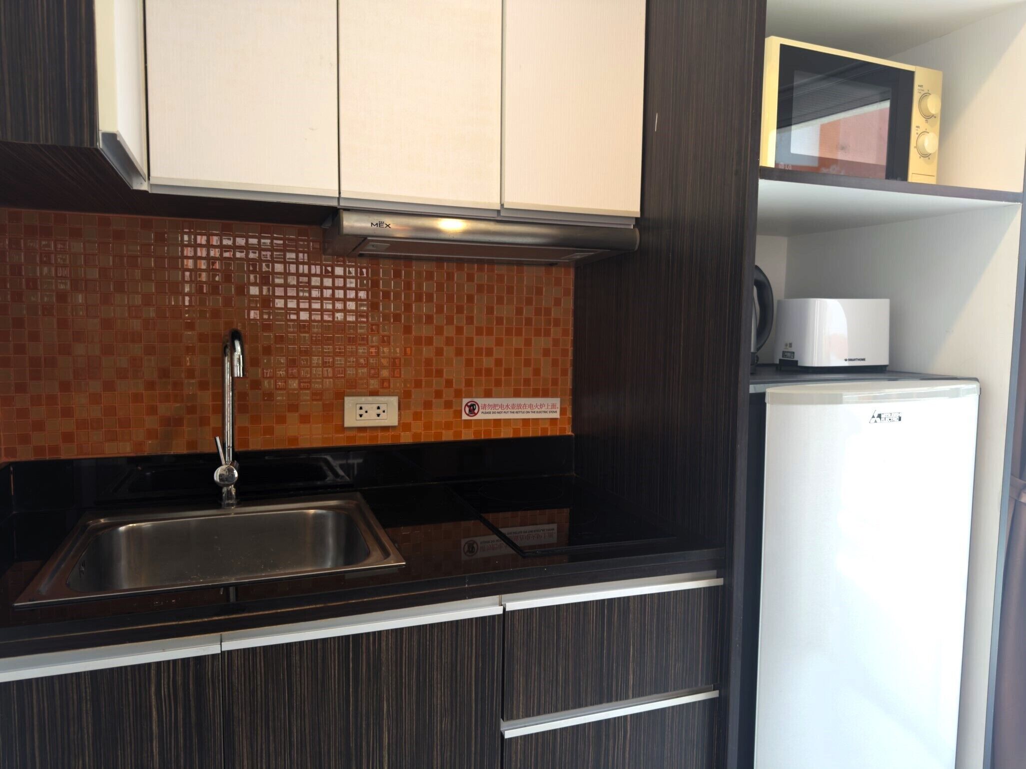 Una cocina con armarios de madera oscura, un lavamanos de acero inoxidable y un refrigerador blanco.
