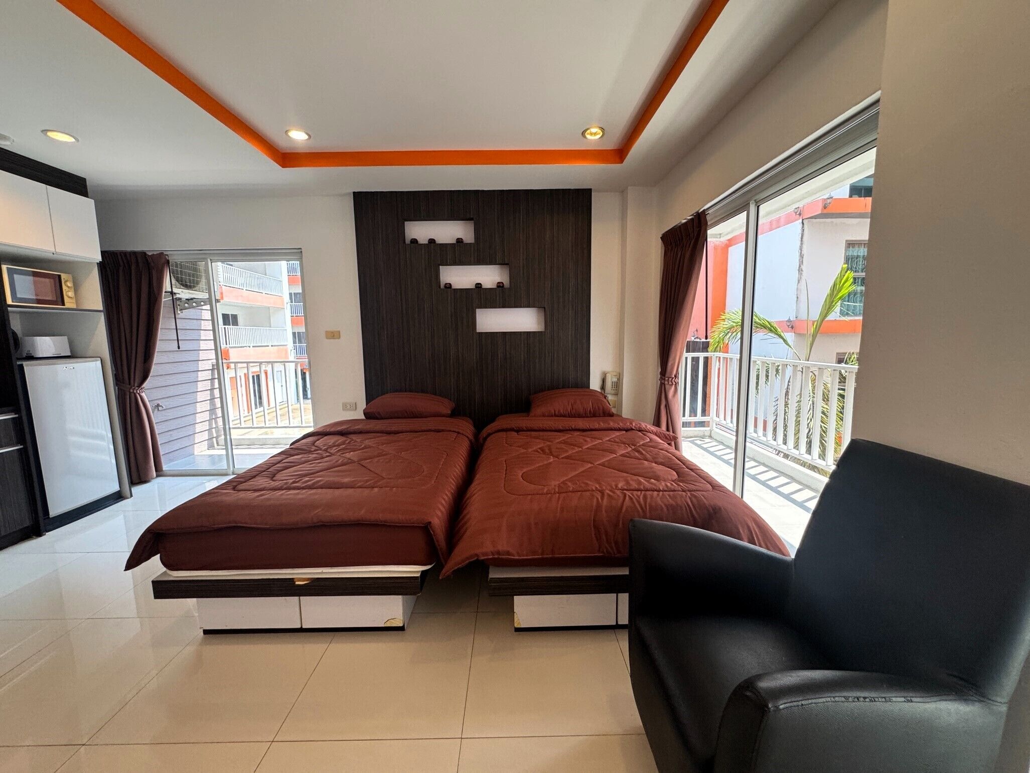 Quarto de hotel com duas camas, uma secretária pequena, uma cadeira, varanda com vista e design moderno com detalhes em laranja.