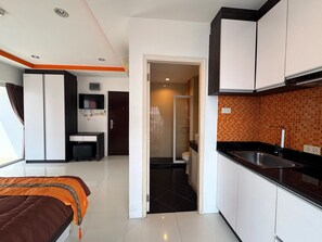 Une chambre d’hôtel de taille réduite, comprenant un lit, un petit bureau, une kitchenette et une salle de bain.