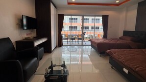 A hotel room with a bed, a desk, a TV, a glass coffee table, and a balcony with a view of buildings. - Pool-View Studio with Balcony - New Nordic VIP 4, Pratumnak (Muang Pattaya)