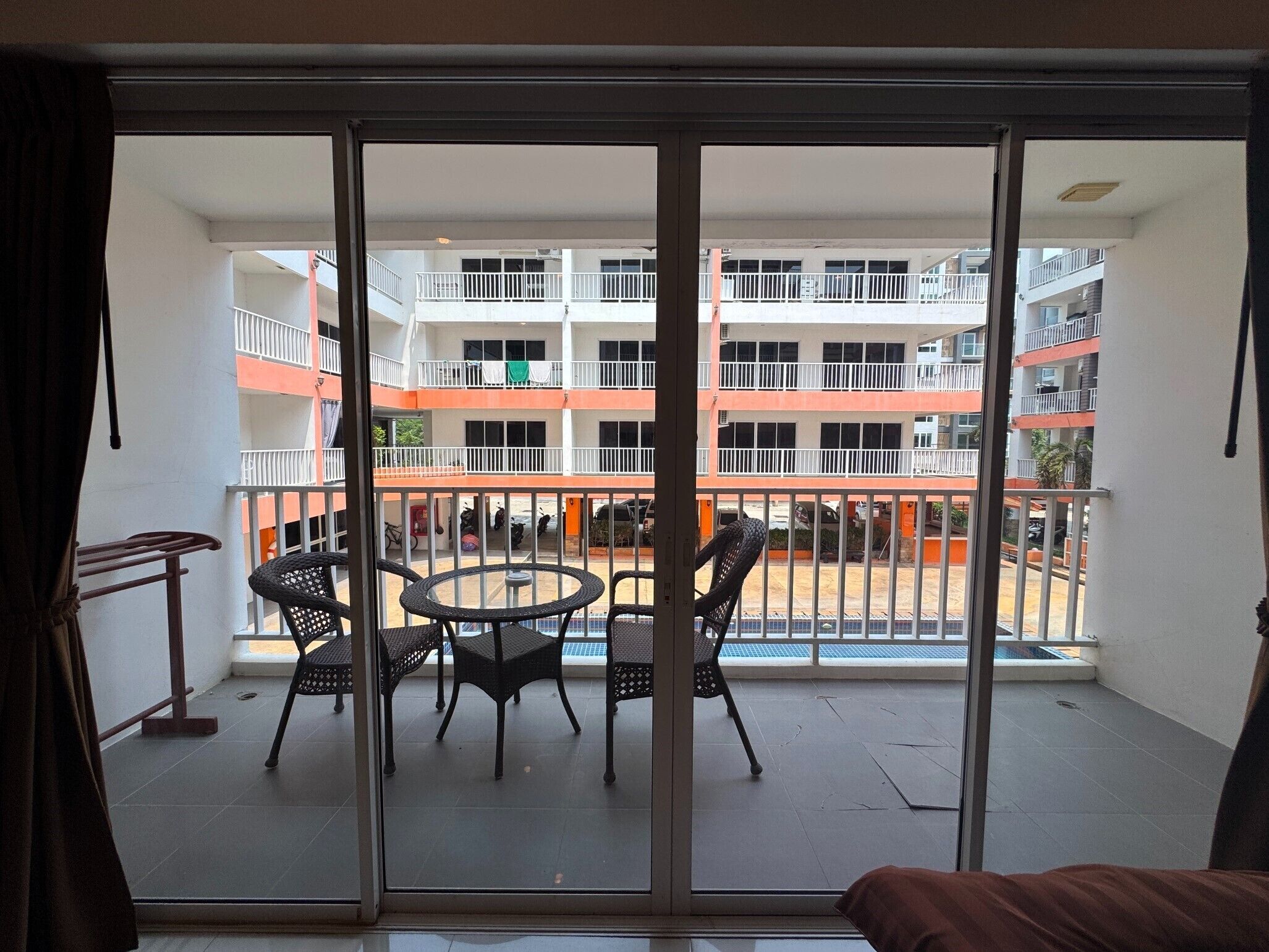 A balcony with a table and chairs, a view of a multi-story building with balconies, and a clear sky.