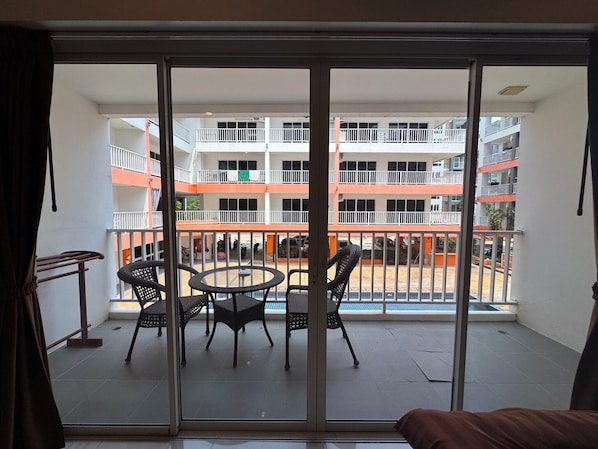 Un balcon avec une table et des chaises, une vue sur un immeuble à plusieurs étages doté de balcons, et un ciel dégagé.