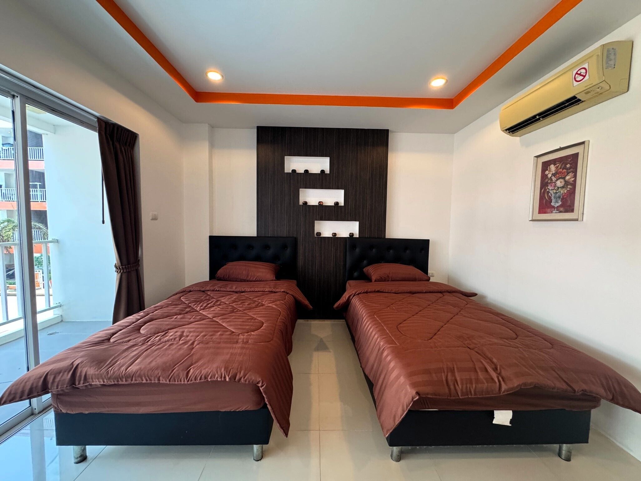 A hotel room with two beds, a large window, a balcony, and a wall-mounted air conditioner.