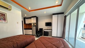 A hotel room with two beds, a kitchenette, a TV, and a balcony with a view. - Comfortable Pool-View Studio with Balcony - Pratumnak, Pattaya (Muang Pattaya)