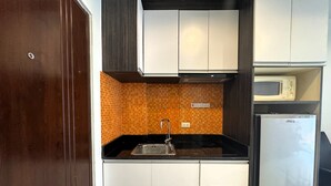 A compact kitchen with white cabinets, a black countertop, a stainless steel sink, a microwave, and a white refrigerator. - Comfortable Pool-View Studio with Balcony - Pratumnak, Pattaya (Muang Pattaya)
