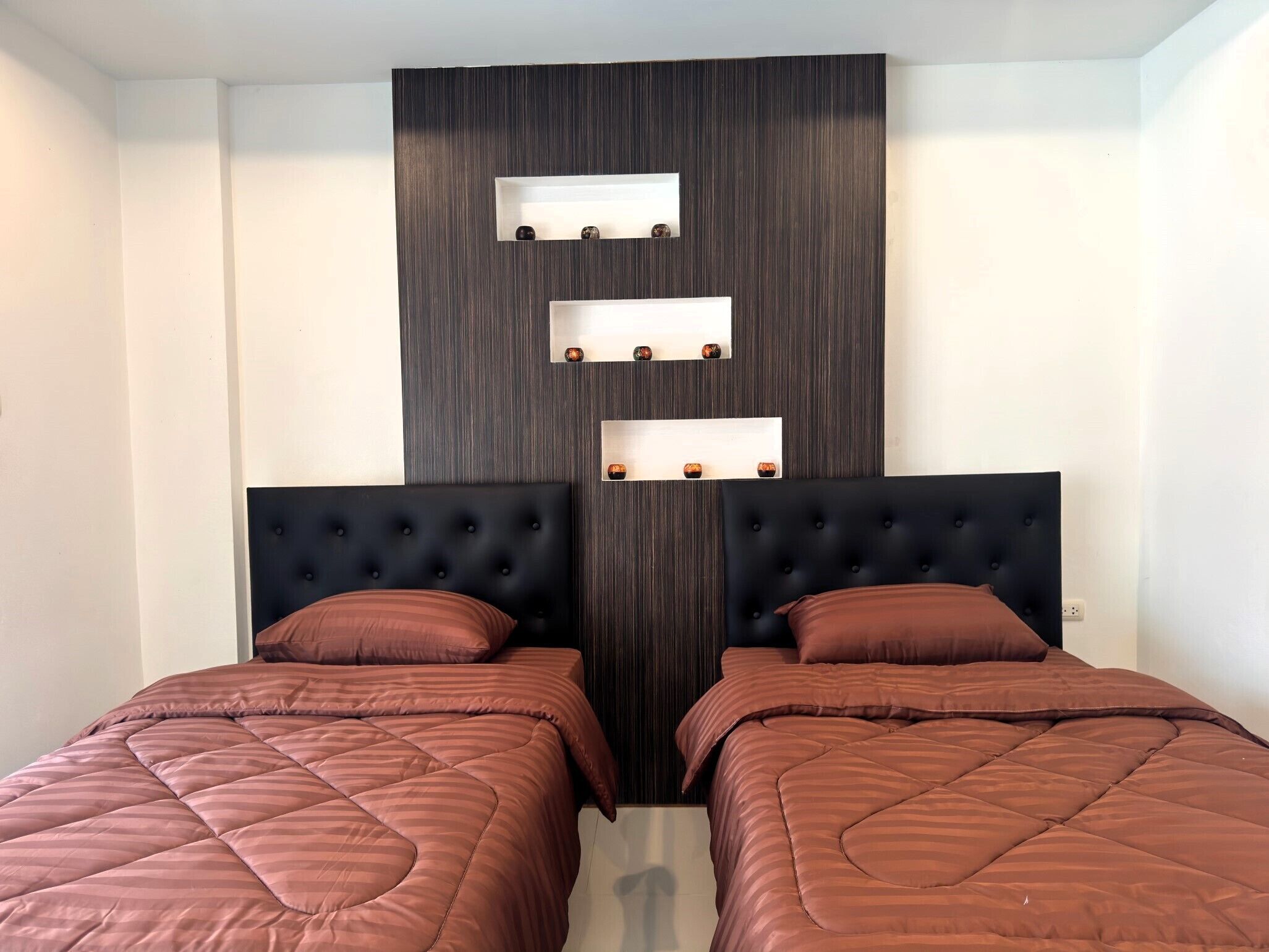 Ein Schlafzimmer mit zwei Betten, dunklen Kopfteilen und einem an der Wand befestigten Regal mit Dekorationen.