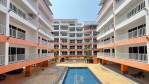 A multi-story building with a central swimming pool, balconies on each floor, and a courtyard with seating areas. - Comfortable Pool-View Studio with Balcony - Pratumnak, Pattaya (Muang Pattaya)
