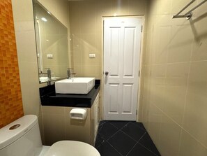 Une petite salle de bain avec des toilettes blanches, un lavabo blanc avec un miroir au-dessus, et une porte blanche.