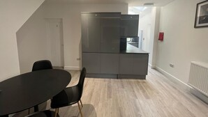 A modern kitchen with grey cabinets and a built-in oven. There is a dining table with black chairs in the foreground. - Deluxe Single Room (Manchester)