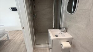 A modern bathroom with a walk-in shower, a sink with a mirror, and a toilet. - Deluxe Single Room (Manchester)