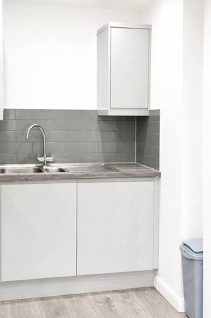 A modern kitchen with a stainless steel sink, white cabinets, and a grey backsplash. - Work-Friendly 1-Bed Leicester (Leicester)