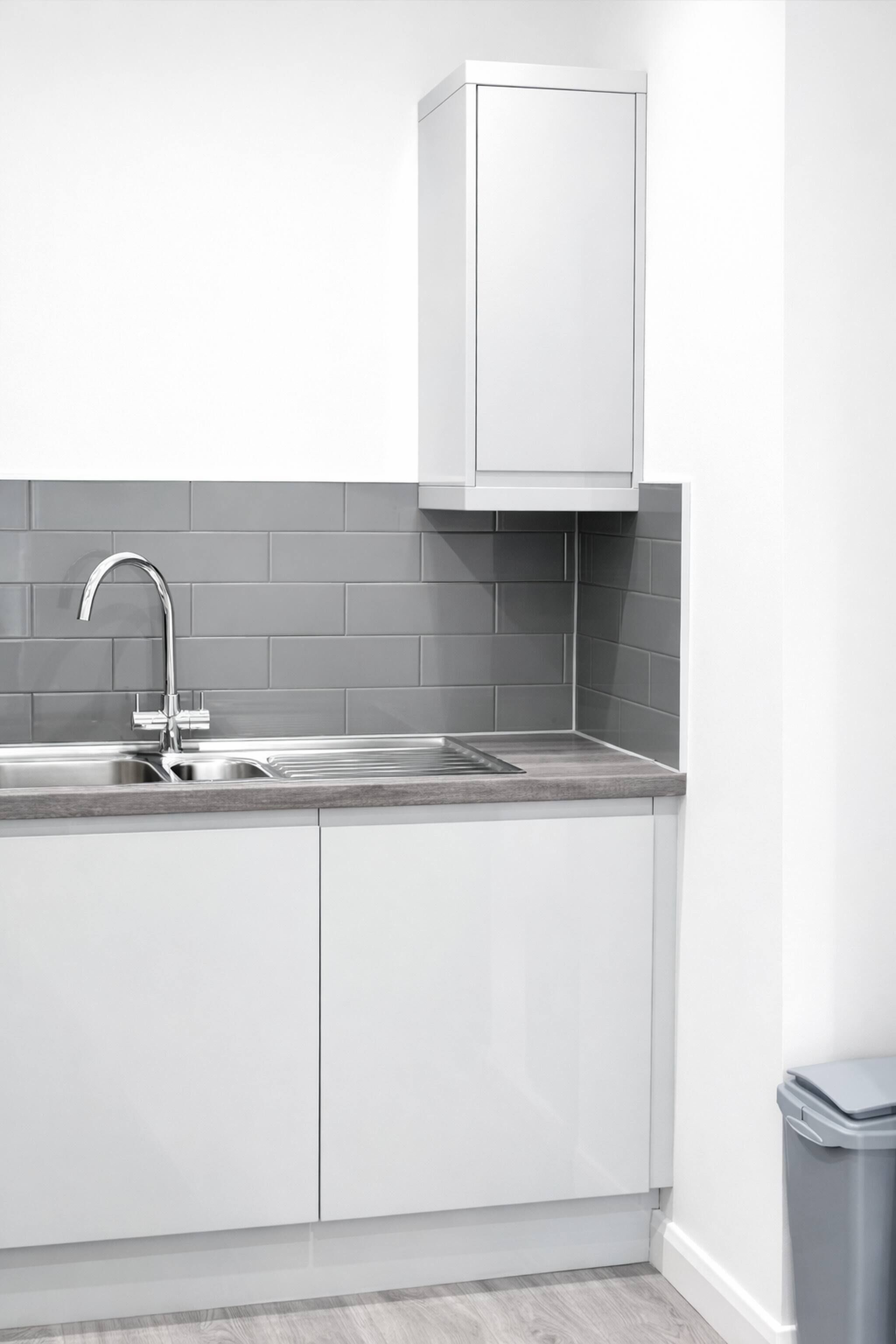 Een moderne keuken met een roestvrijstalen spoelbak, een grijze betegelde achterwand en witte kastjes.