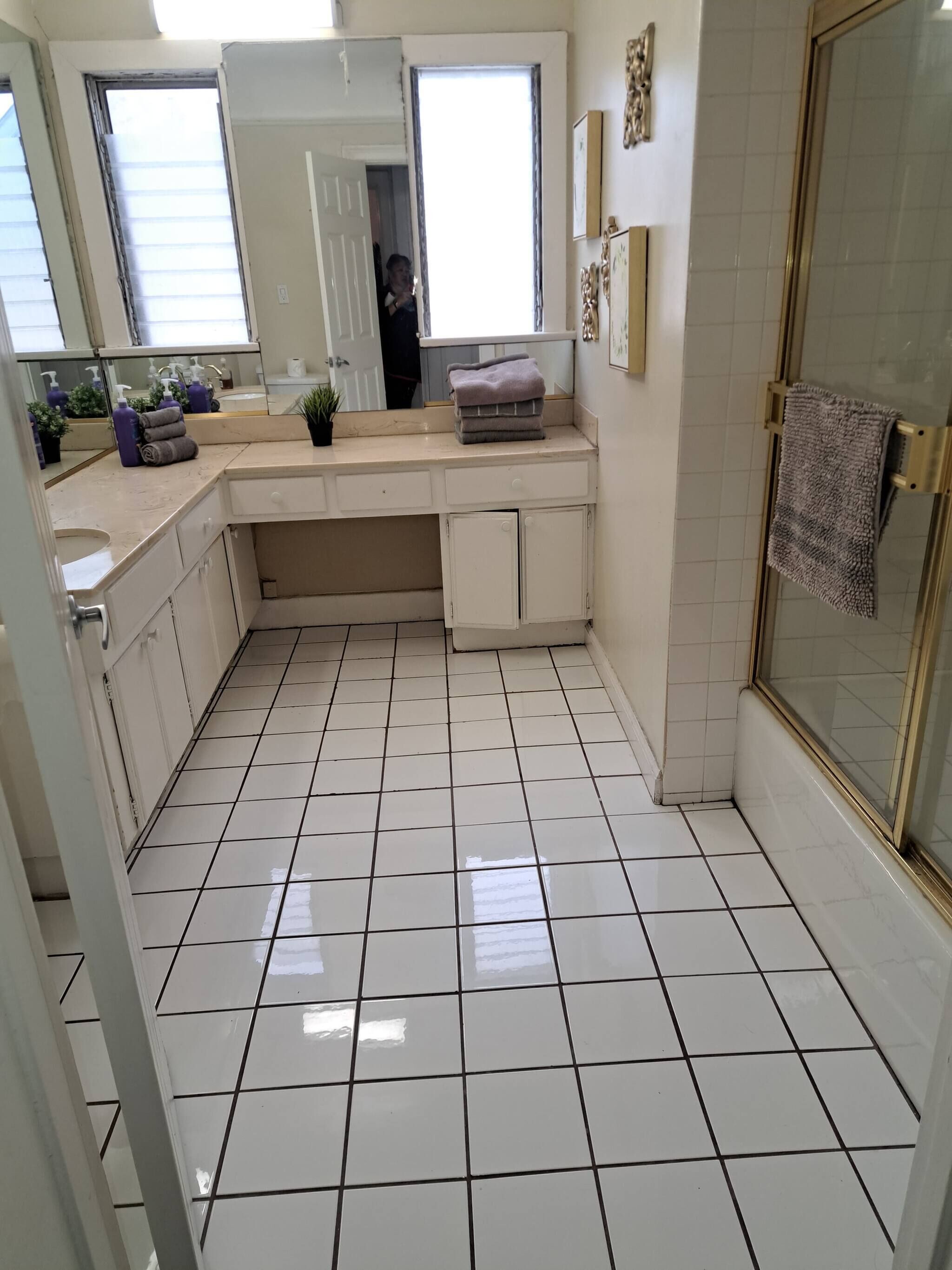 A bathroom with white tiled floors, a sink, a vanity with a mirror, and a shower area.
