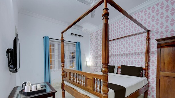 A four-poster bed with a wooden frame and a white mattress, a small table with a glass top, and a wooden wardrobe. - Collection O Sunrise Point Serenity Beach (Vanur)
