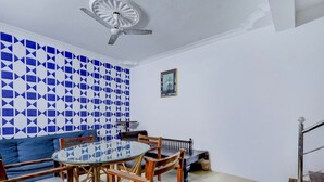 A dining area with a round glass table, wooden chairs, a blue and white patterned wall, a ceiling fan, and a small framed picture on the wall. - Collection O Sunrise Point Serenity Beach (Vanur)