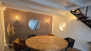 Ein moderner Essbereich mit einem runden Holztisch, umgeben von Stühlen, einer Wand mit vertikalen Lamellen und einer Treppe im Hintergrund.