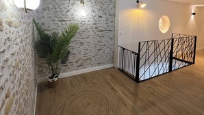 Ein geräumiger Raum mit freiliegenden Holzbalken, einer Steinwand und Holzdielen. Eine Topfpflanze und ein runder, gewebter Teppich sind ebenfalls vorhanden.