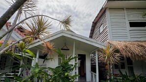 A white house with a covered porch, surrounded by tropical plants and a thatched roof. - Habana Hotel  (Kuta)