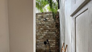 A bathroom with a stone wall, a toilet paper holder, and a wooden ladder leaning against the wall. - Habana Hotel  (Kuta)