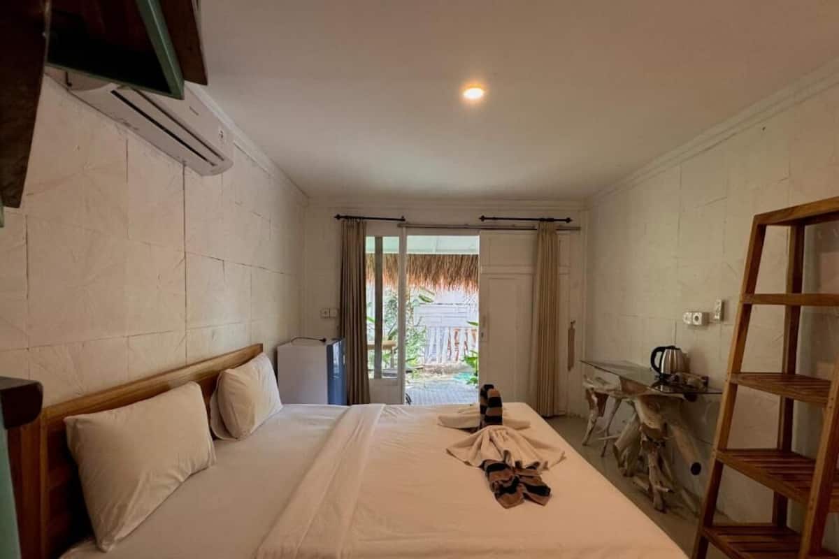 A hotel room with a bed, a wooden headboard, a small table with a kettle, and a wooden shelf.