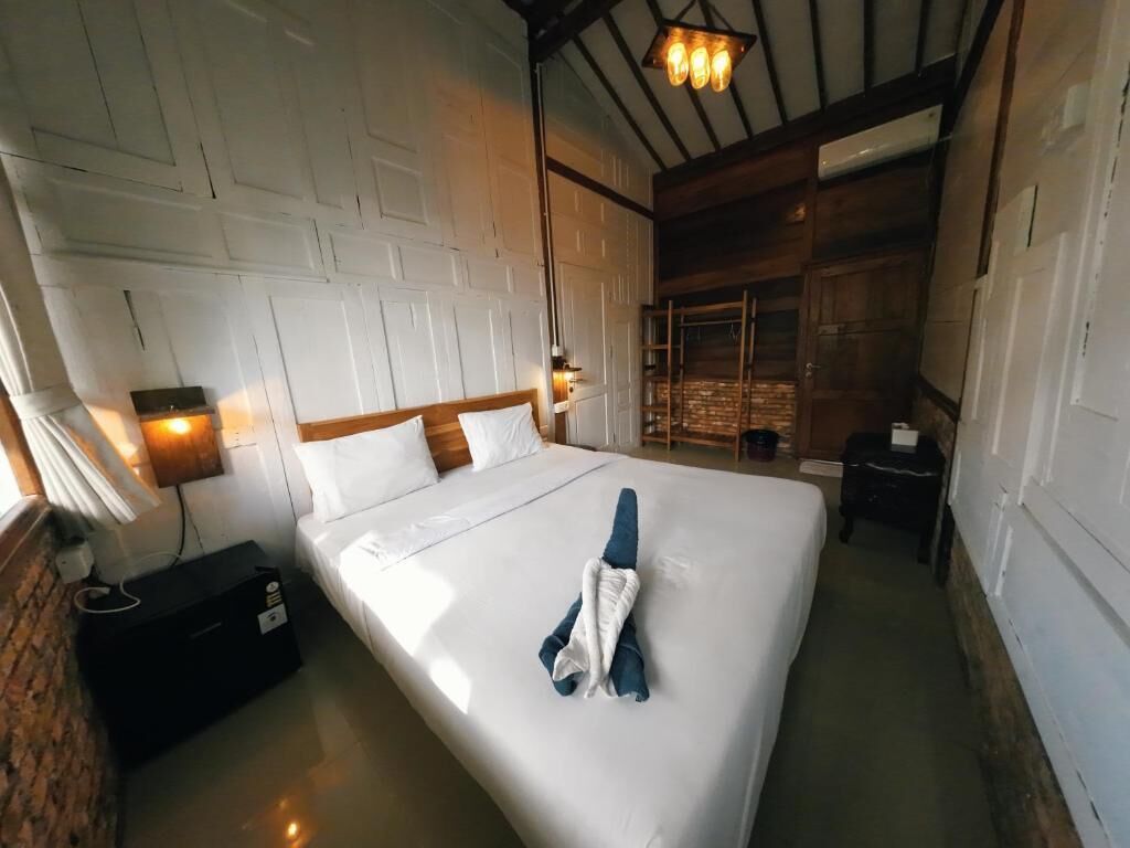 A hotel room with a large bed, a wooden headboard, a nightstand, a lamp, and a brick wall.