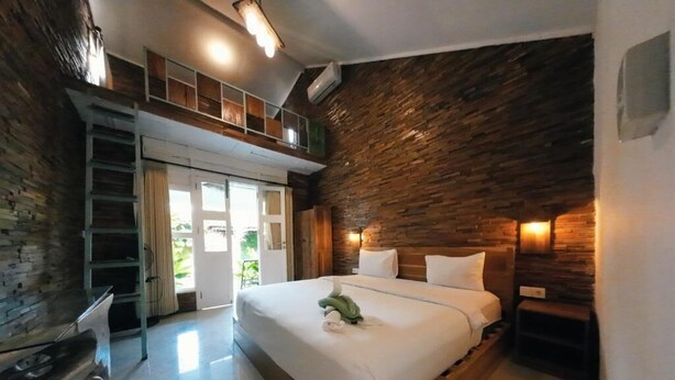 A bedroom with a wooden bed, a loft area, and a stone wall. - Habana Hotel  (Kuta)