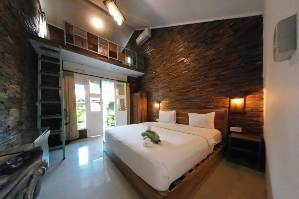 A bedroom with a wooden bed, a loft area, and a stone wall.