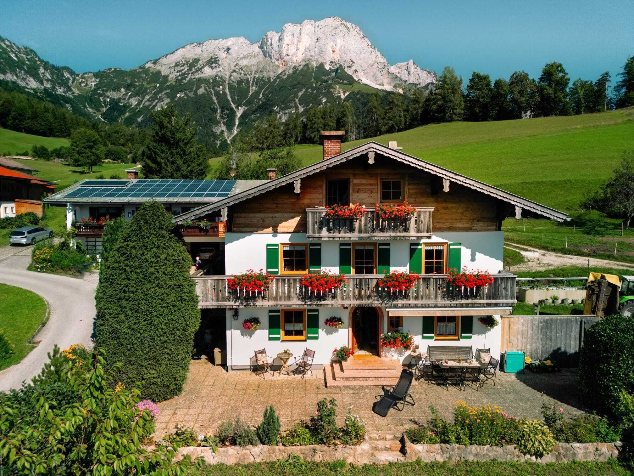 Een chalet met twee verdiepingen, een balkon, zonnepanelen en uitzicht op bergen.