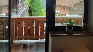 Un balcone con vista su un paesaggio montano, ringhiere in legno e una pianta in vaso.