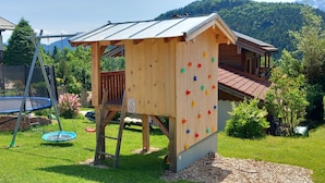 Una casetta in legno con una parete da arrampicata e un trampolino in un giardino.