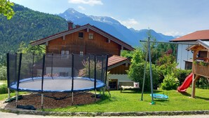 Una casa in legno con un trampolino e uno scivolo nel giardino, circondata dalle montagne.