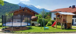 Una casa de fusta amb un trampolí i un tobogan al pati, envoltada de muntanyes.