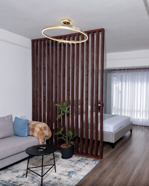 Ein modernes Zimmer mit Sofa, einem kleinen Tisch, einer Topfpflanze, einem Bett und einem Holztrenner.