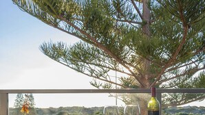 A balcony with a table, two wine glasses, and a bottle of wine. - Relaxing three bedroom Beach House on the coast. Close to cafes and golf course. (Secret Harbour)