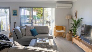 A living room with a grey sofa, a coffee table, a television, and a plant. - Relaxing three bedroom Beach House on the coast. Close to cafes and golf course. (Secret Harbour)