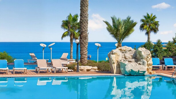 Ein Pool mit Liegestühlen, Palmen und Blick auf das Meer.