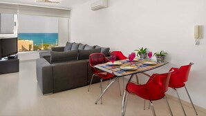 Ein modernes Wohnzimmer mit einer Couch, einem Esstisch, roten Stühlen und Meerblick.