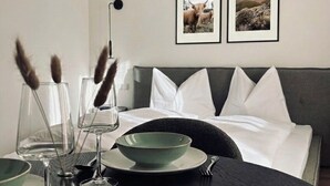 Un coin repas bien aménagé, avec une table dressée pour deux personnes, un lit avec une literie blanche et deux tableaux encadrés au mur.