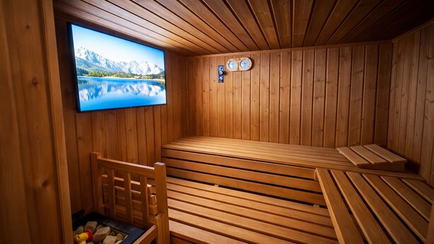 Un sauna avec des bancs en bois, un téléviseur diffusant un paysage pittoresque et une horloge au mur.