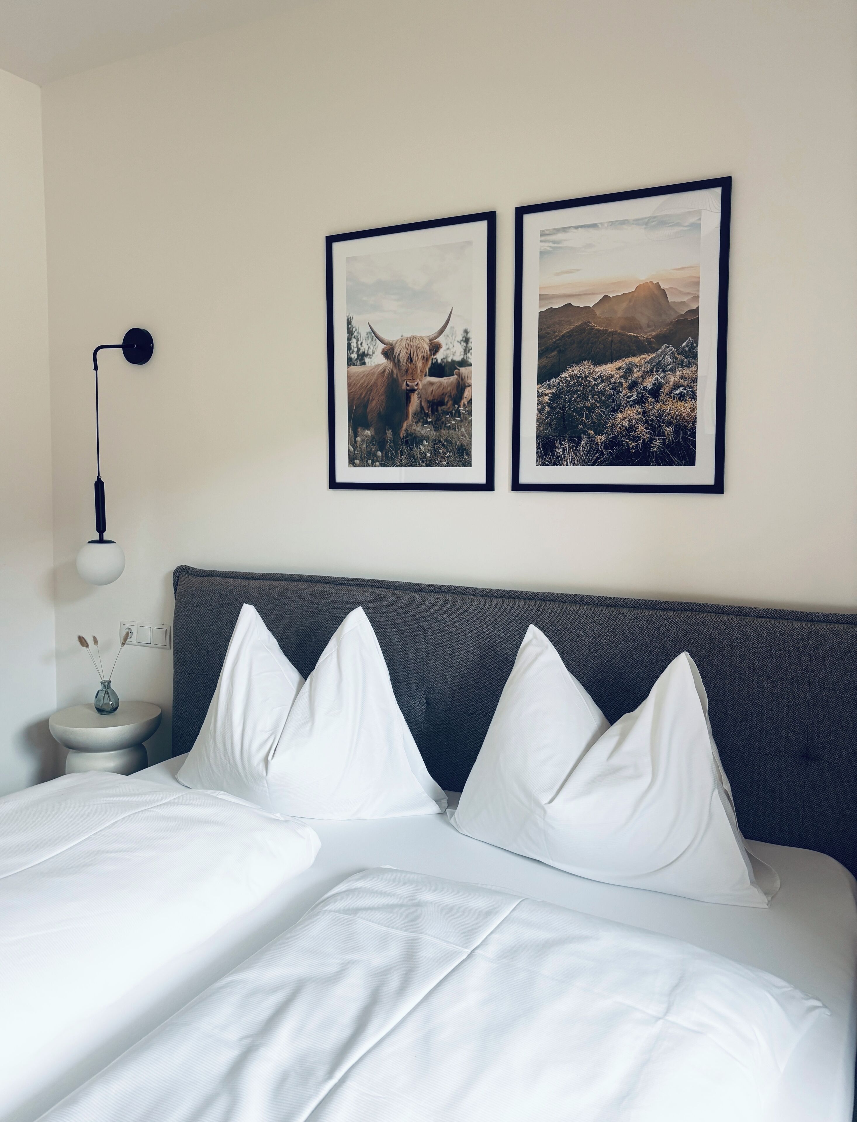 A bed with white bedding, a gray headboard, and two framed pictures on the wall.