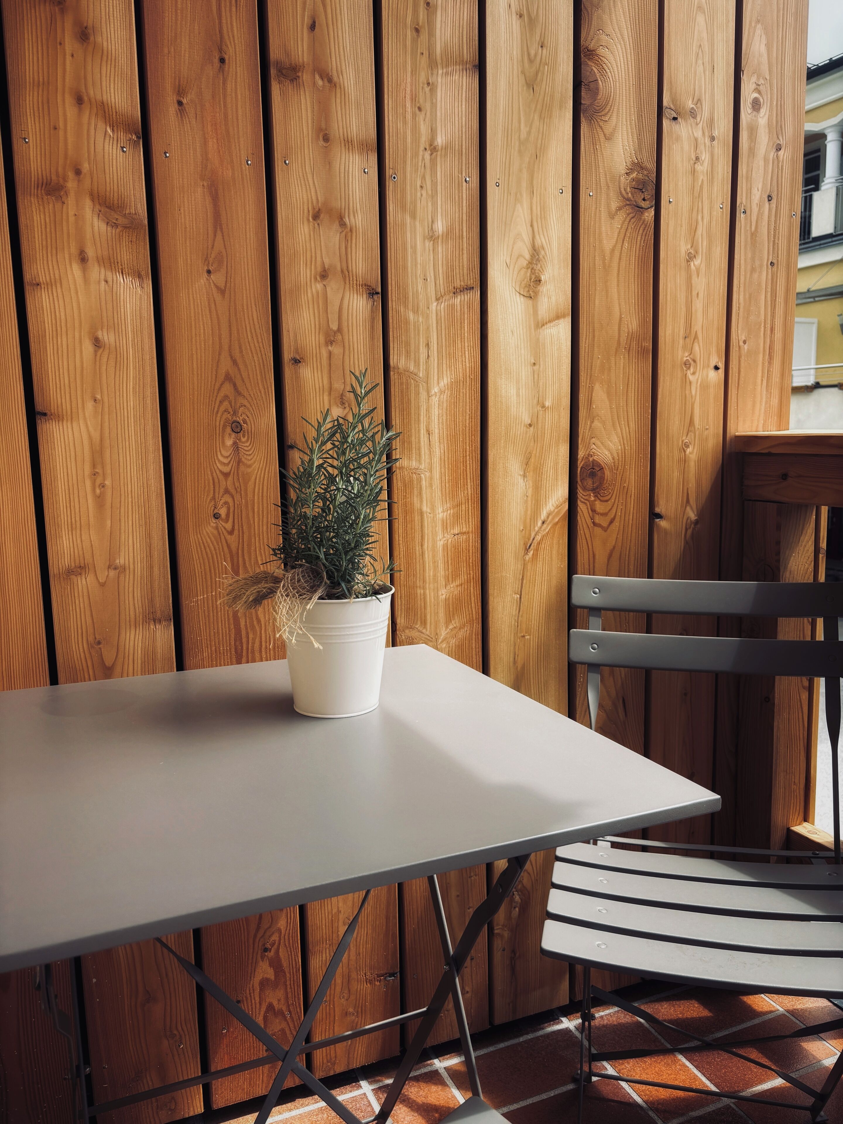 A table with a potted plant, a chair, and a wooden fence in the background.