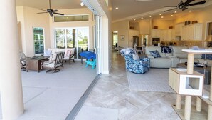 A spacious living area with a large sofa, a coffee table, and a cat tree. There is a kitchen area with cabinets and a refrigerator in the background. - Waterfront, Private Pool, Close to Beaches, Best of Marco! (Marco Island)